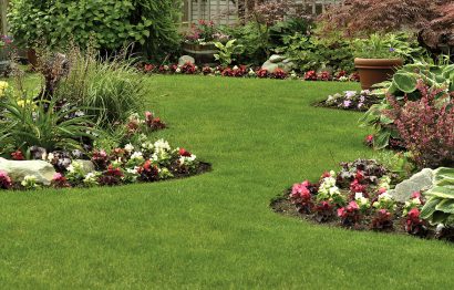 A beautifully arranged flower garden and residential yard on a bright day.